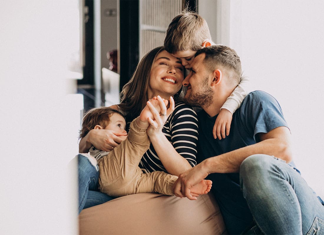 About Our Agency - Portrait of a Happy Family with Two Young Children Having Fun Spending Time Together While Sitting in the Living Room
